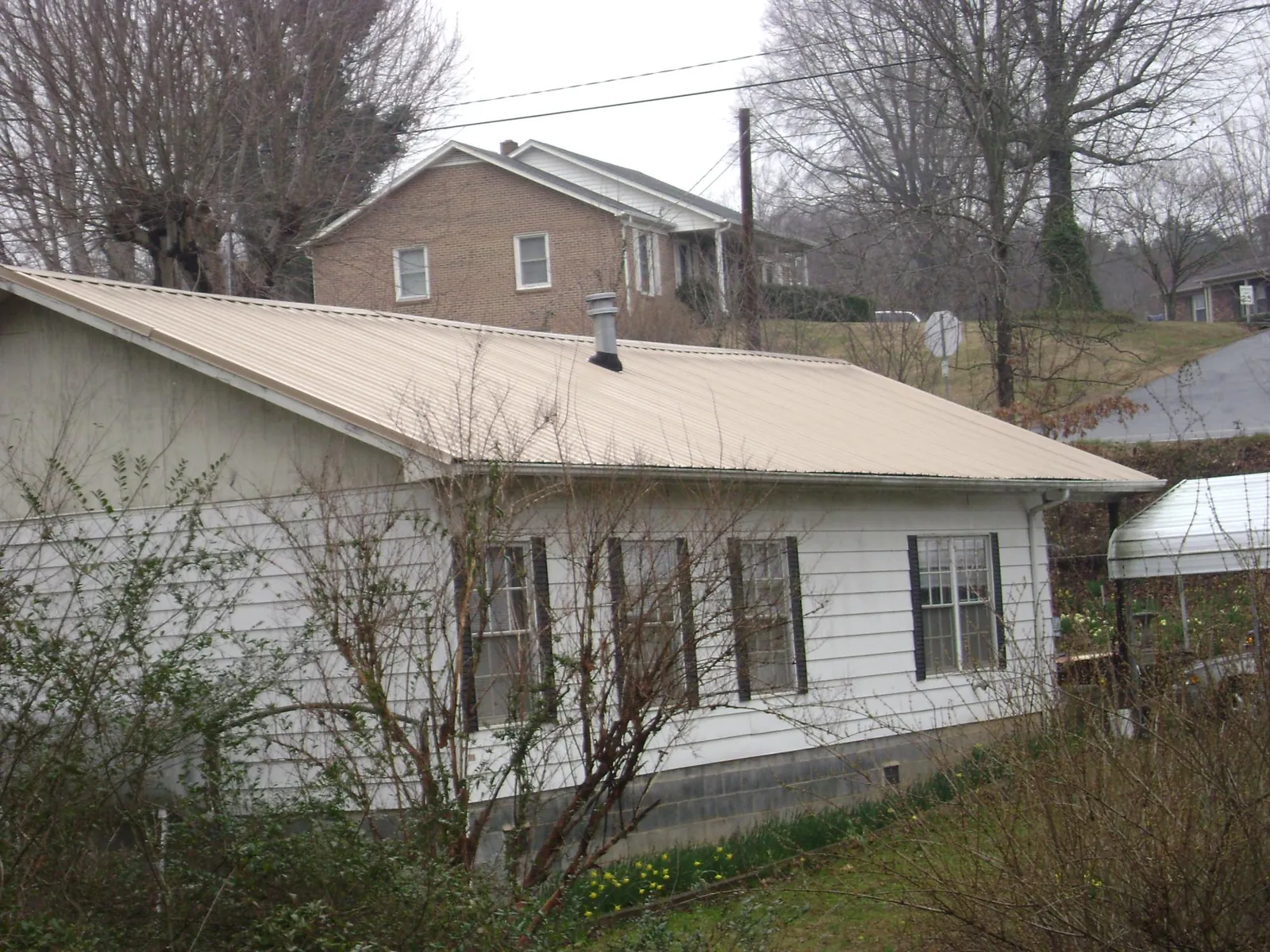 Tan metal roof on a white sided house set into a hillside — Commercial Roofing by Roofing Brothers in Hebron