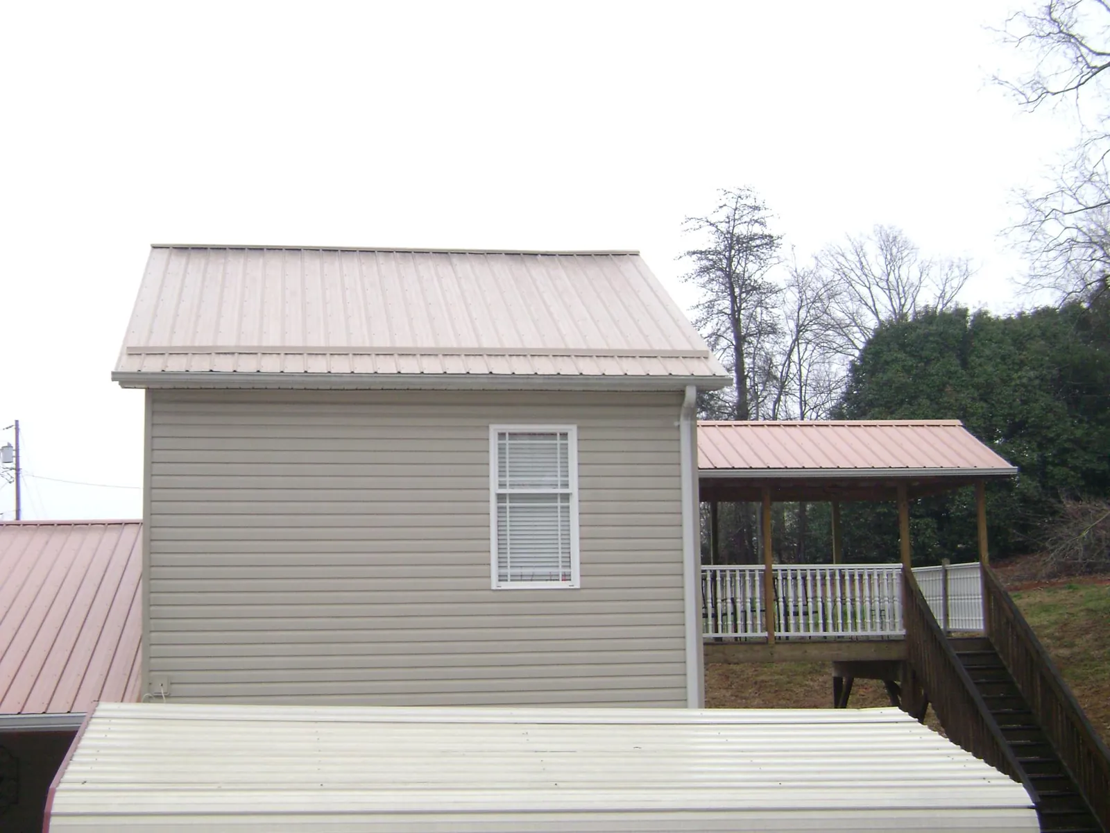 Tan metal roofs on a two story addition and attached porch, from a Roof Replacement job in Hebron